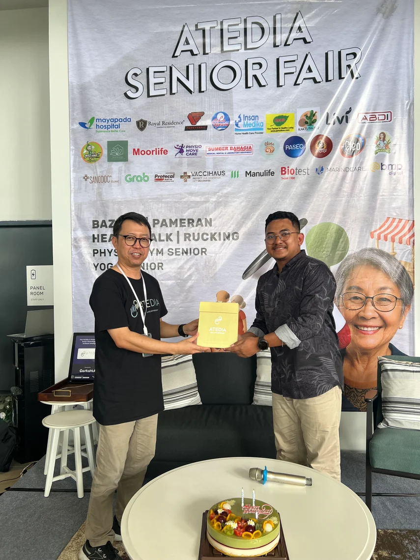 A handover in front of the ATEDIA Senior Fair backdrop, with the fair's partner logos behind